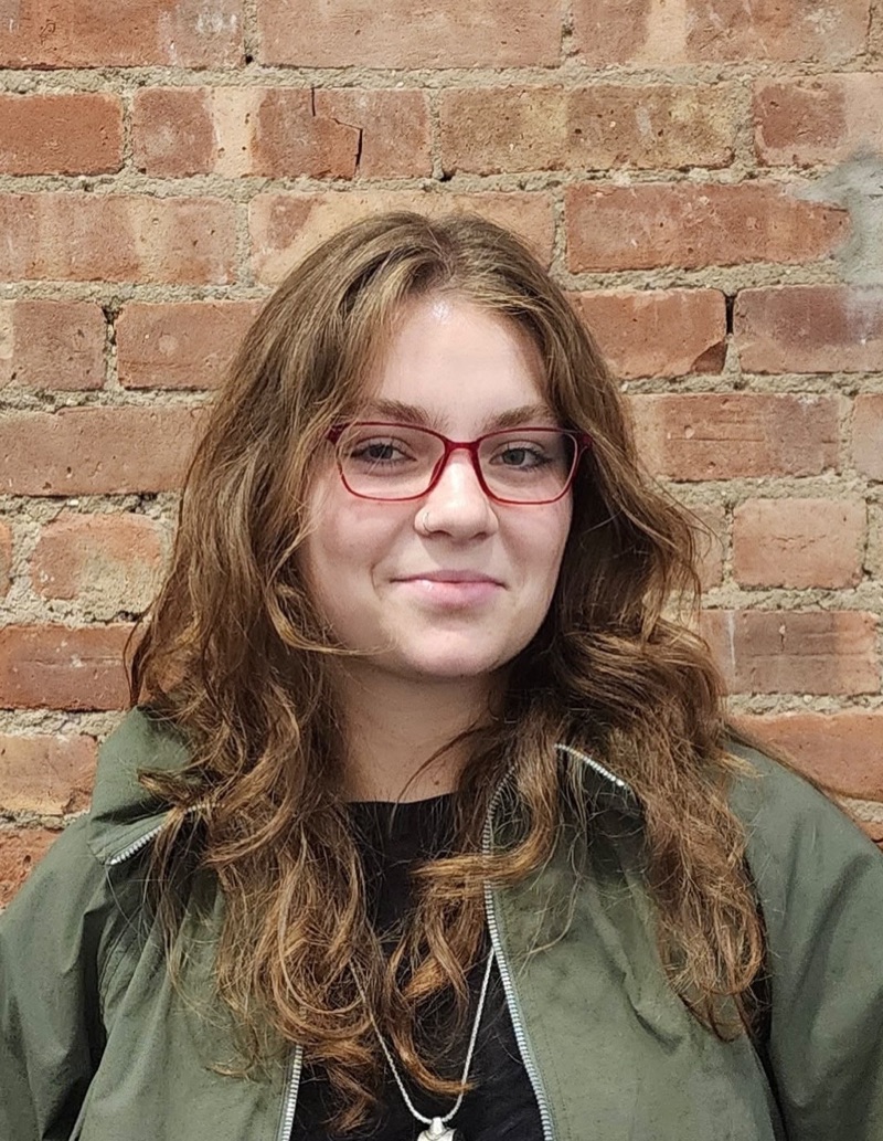 Sasha Getz in red glasses, smiling in front of a brick wall